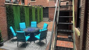 Ein Backsteinhaus mit Feuerleiter, einer kleinen Terrasse mit gemustertem Teppich und einem Tisch mit Stühlen.