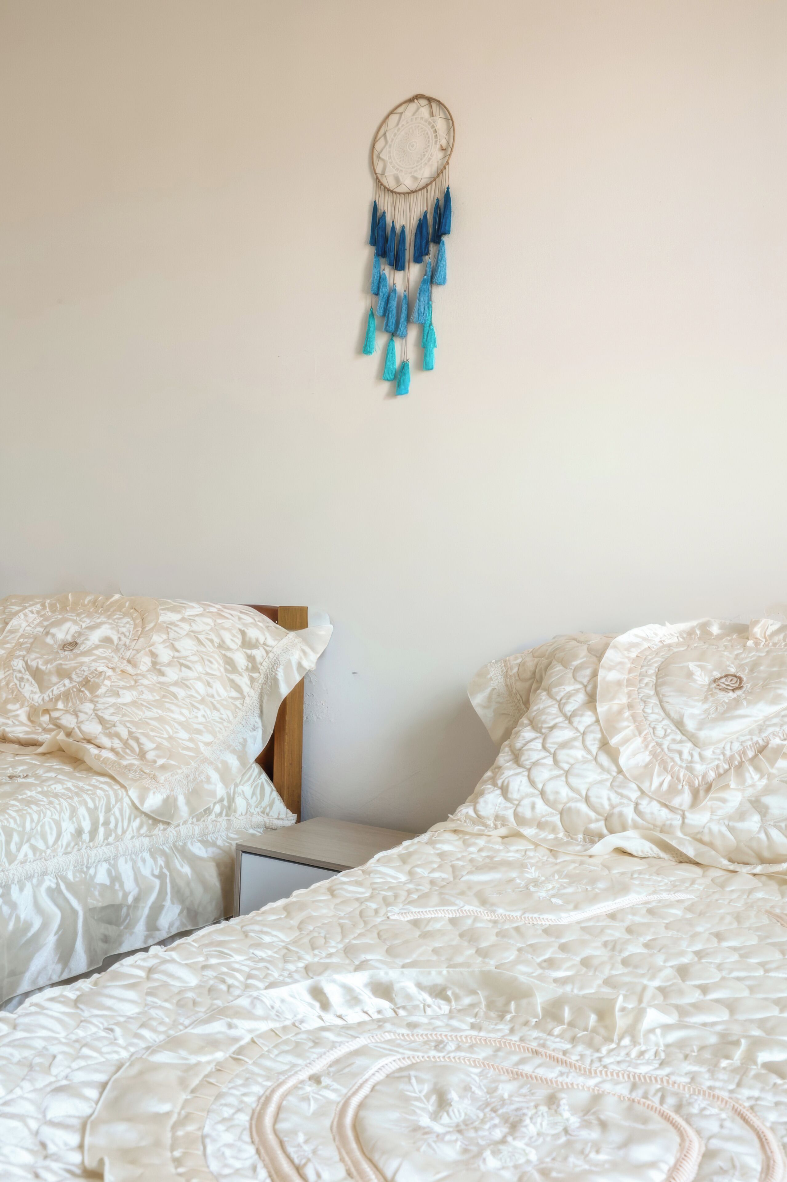 A bedroom with two beds, a nightstand, and a dreamcatcher on the wall.