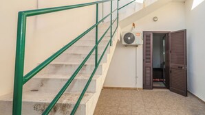 A staircase with green railings, a door with a brown shutter, and an air conditioning unit mounted on the wall. - Casa Clale (Marina di Pescoluse)