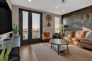 A living room with a leather sofa, a coffee table, a TV, and a large window with a view. - The Urban Cowboy (Nashville)