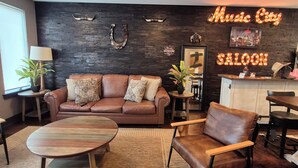 A modern living room with a sofa, armchairs, a coffee table, a ceiling fan, and a neon sign reading 'Music City Saloon.' - The Urban Cowboy (Nashville)