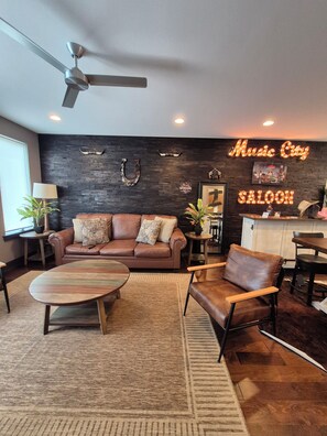 A modern living room with a sofa, armchairs, a coffee table, a ceiling fan, and a neon sign reading 'Music City Saloon.' - The Urban Cowboy (Nashville)