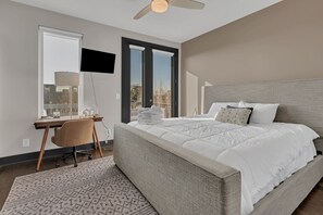 A bedroom with a bed, a desk, a chair, a TV, and a window with blinds. - The Urban Cowboy (Nashville)