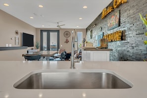 A modern kitchen with a stainless steel sink, a dining area with a table and chairs, and a living space with a sofa and a television. - The Urban Cowboy (Nashville)