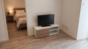 Ett sovrum med en säng, en tv på ett vitt tv-bord och ett nattduksbord med en lampa.