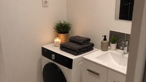 Ett litet och praktiskt tvättrum med tvättmaskin, handfat och en liten krukväxt.