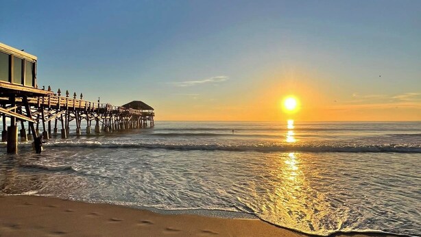 A beach with a pier extending into the water, a sunset, and footprints in the sand. - STUNNING! 1 Bedroom Panoramic Ocean View! Beach Cottage Feel, Steps to Shore! (Cocoa Beach)