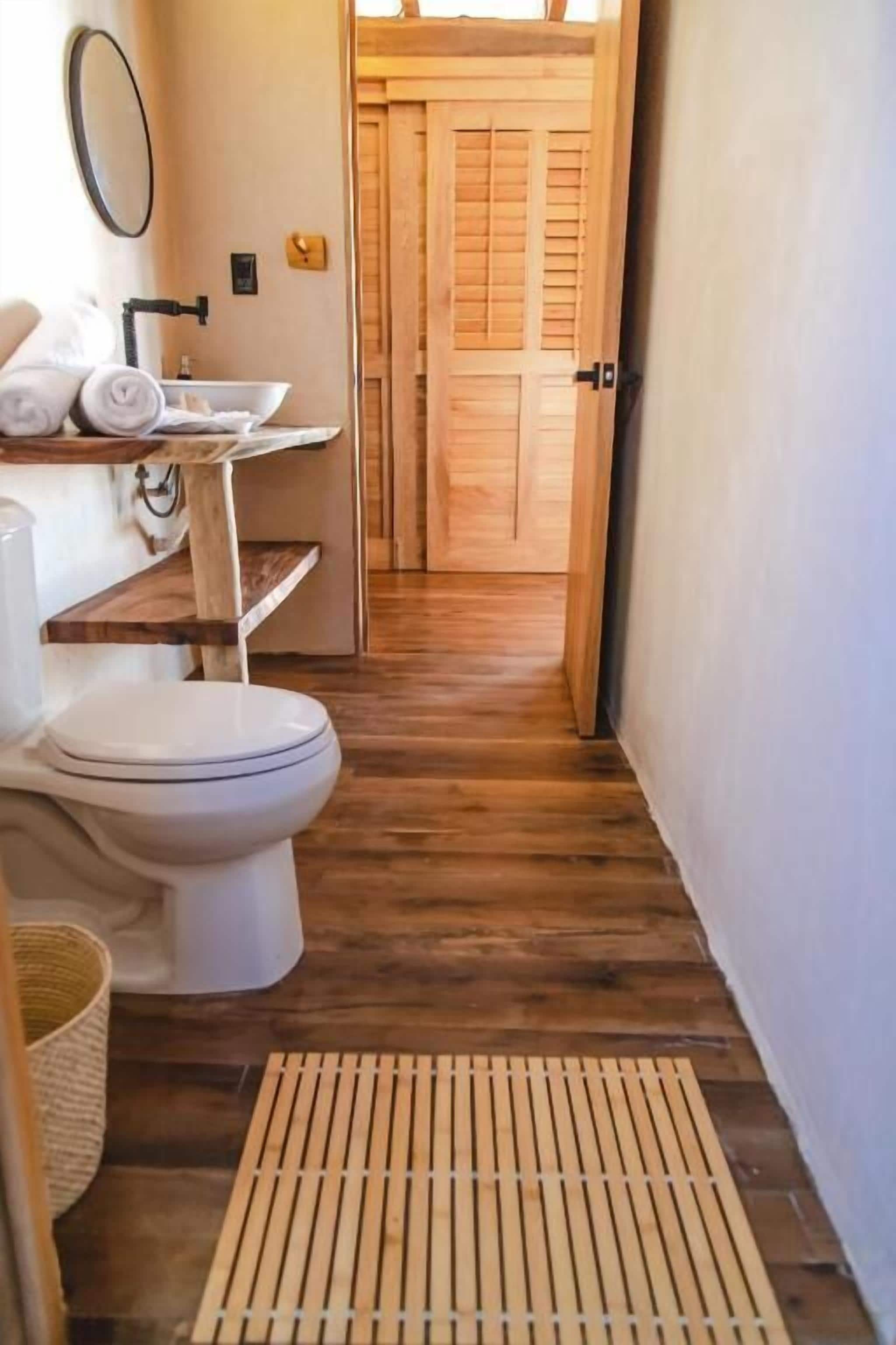 A bathroom with a toilet, sink, and wooden floor.