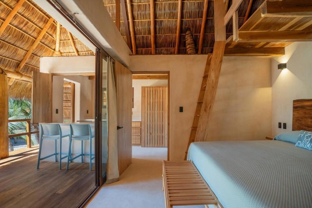 A modern bedroom with a large bed, a glass door leading to a balcony, and a wooden ceiling.