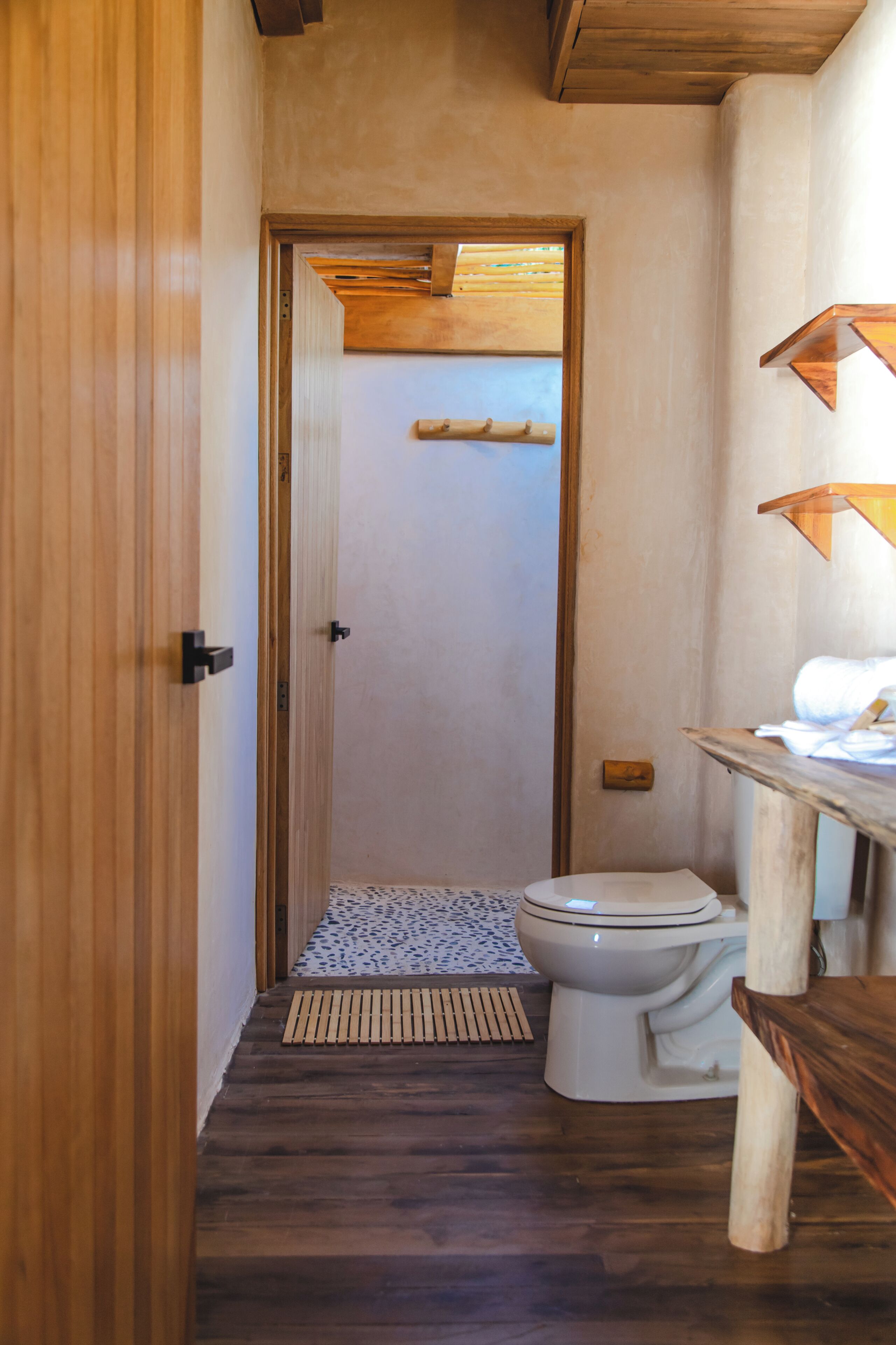 Un corridoio stretto con una porta in legno, un bagno e un piccolo ripiano in legno con degli asciugamani.