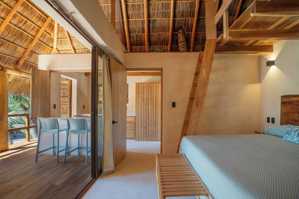 Un dormitorio con una cama, un banco de madera y una zona de estar con sillas.