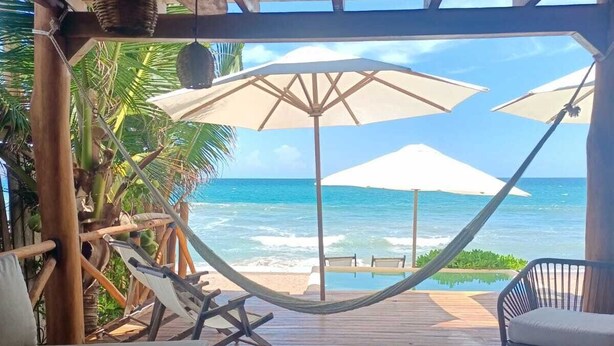 A wooden deck with a hammock, lounge chairs, and an umbrella overlooking the ocean. - Mangle Rojo Palafitos (Boca de Iguanas)