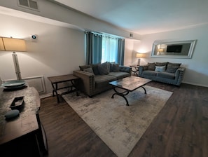 Un salon avec deux canapés, une table basse, une table d’appoint et une lampe.