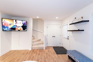 Ein modernes Wohnzimmer mit Flachbildfernseher, einer Treppe, einer Tür und einer Bank.