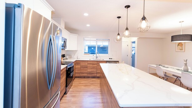 Una cucina moderna con una grande isola, elettrodomestici in acciaio inossidabile, mobili in legno e illuminazione a sospensione.