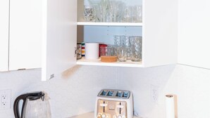 Una cucina con un pensile bianco contenente bicchieri, un tostapane e un bollitore.