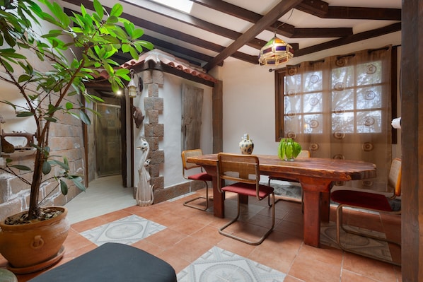A patio with a wooden table and chairs, a potted plant, and a tiled floor.