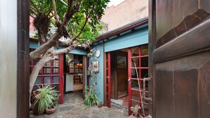 A narrow courtyard with a tree, potted plants, and a blue building with red doors. - Vacation Home 'Casa Afrikika' with Sea View, Private Terrace and Wi-Fi (Las Cruces)