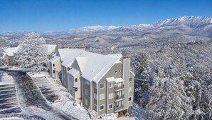 A residential building complex with multiple apartment buildings, a snow-covered landscape, and distant mountains.