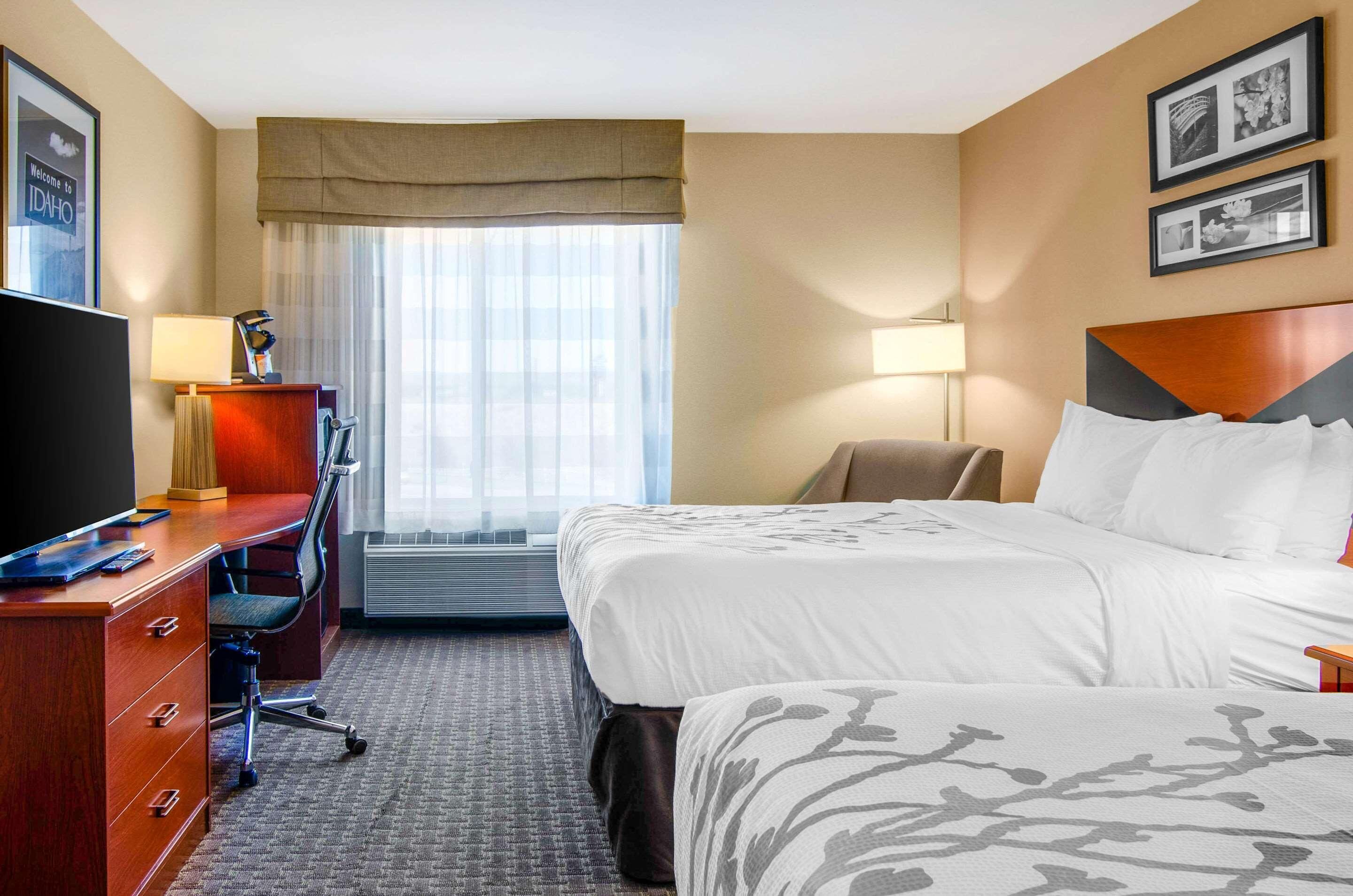A hotel room with a bed, a desk with a chair, a TV, and a window with curtains.