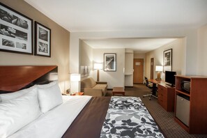 Una habitación de hotel con cama, escritorio, silla, televisor y lámpara de escritorio.