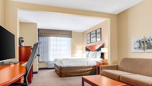 Une chambre d’hôtel comprenant un lit, un bureau avec un ordinateur, une télévision, un canapé et une fenêtre avec des rideaux.