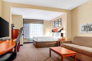 Una habitación de hotel con cama, escritorio, televisor, sofá y ventana con cortinas.