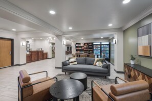 Un amplio salón con sofá, sillones, una mesa de centro y una estantería llena de libros y objetos decorativos.