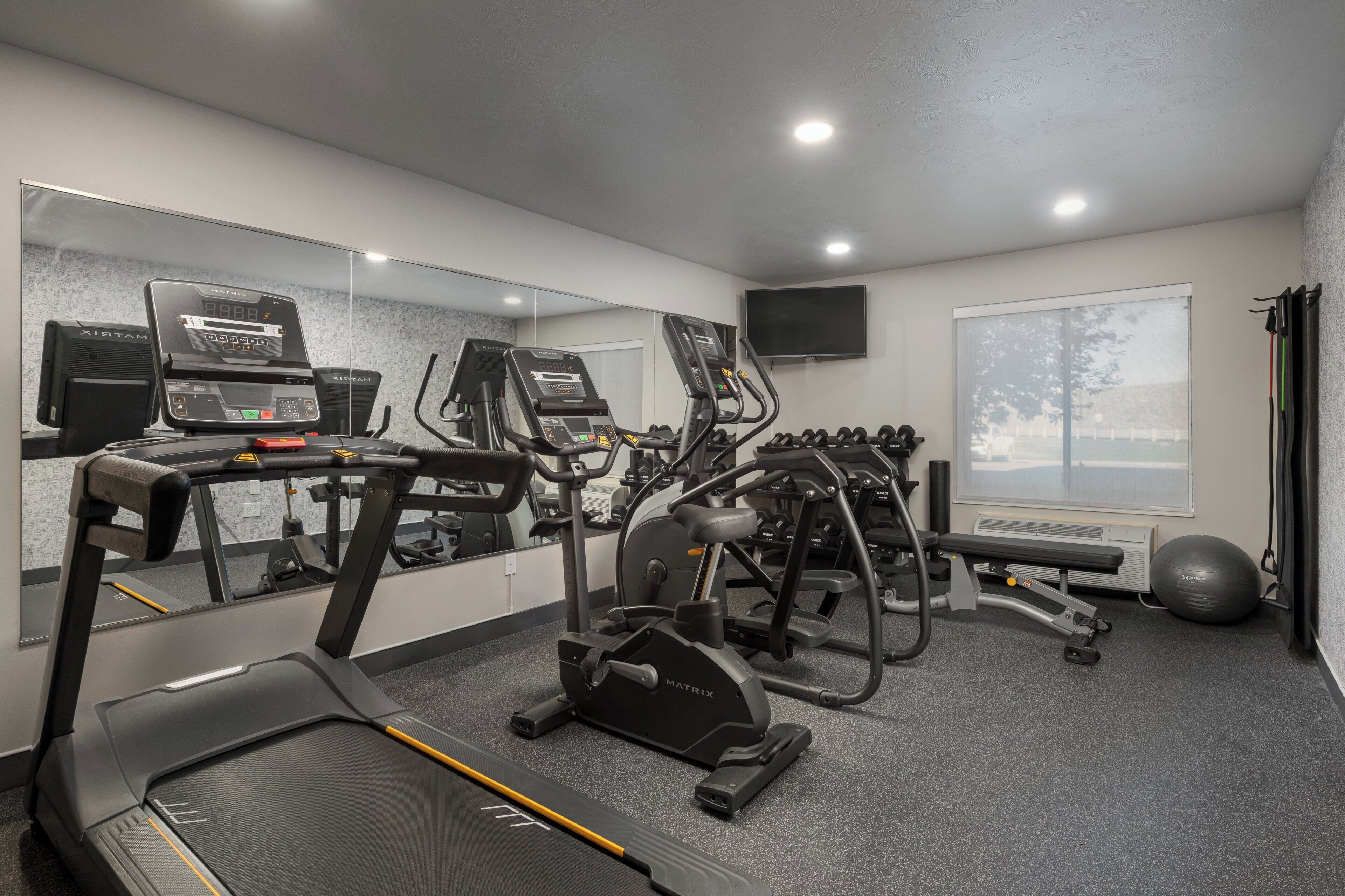 Un gimnasio con cintas de correr, elípticas y un espejo grande.
