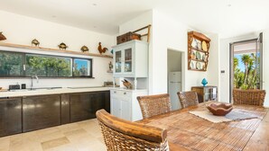 A modern kitchen with dark cabinets, a white island, and a dining area with a wooden table and wicker chairs. - Villa Aspri Luxury by Perle di Puglia (Carovigno)