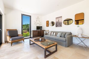 Sala de estar com uma cadeira de vime, um sofá cinza, uma mesa de centro de madeira e uma televisão.