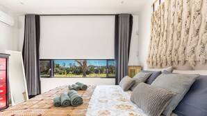 A bedroom with a large bed, a view of greenery outside, a red dresser, and a window with curtains. - Villa Aspri Luxury by Perle di Puglia (Carovigno)