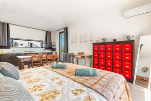 Quarto de hotel moderno com cama grande, área de jantar, cozinha e um móvel de armazenamento vermelho.