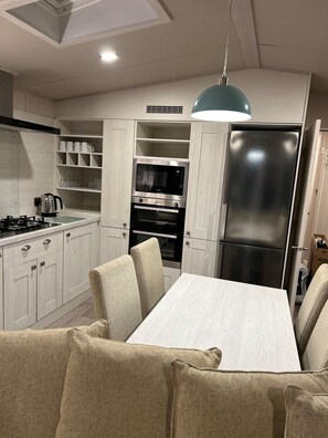 Una cocina moderna con armarios blancos, horno empotrado, refrigerador de acero inoxidable y un comedor con mesa y sillas.