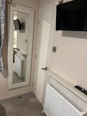 Habitación de hotel con puerta, espejo, radiador y televisor montado en la pared.