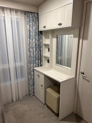 Habitación de esquina con armario empotrado, tocador con espejo y un pequeño banco.