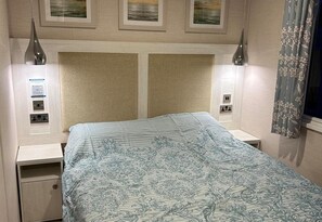 A hotel room with a bed, bedside tables, a headboard with artwork, and a window with curtains.