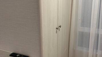 A wooden wardrobe with two doors and a remote control on the floor beside it.