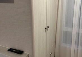 A wooden wardrobe with two doors and a remote control on the floor beside it.