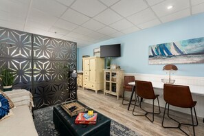 A modern living room with a sectional sofa, a coffee table, a TV, and a dining area with chairs. - "Co-Sea Casa" - Short Stroll from the Sandy Shores! (Carolina Beach)