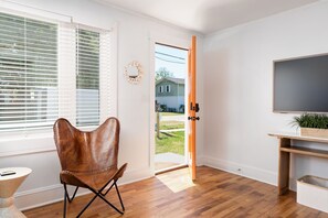 Ein Zimmer mit Holzboden, einem braunen Ledersessel, einem Fernseher auf einem Holzgestell und einer zur Außenseite führenden Tür.