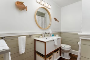 Une salle de bain avec un miroir rond, un lavabo, des toilettes et un porte-serviettes.
