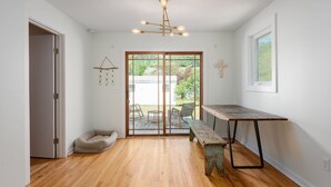 Een kamer met houten vloeren, een bank, een tafel, een hanglamp en een schuifdeur naar buiten.