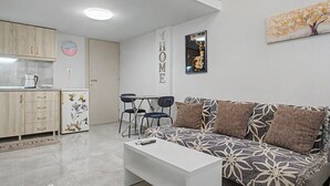 Un espace de vie moderne comprenant un canapé, une table basse et un coin cuisine avec des placards et un réfrigérateur.