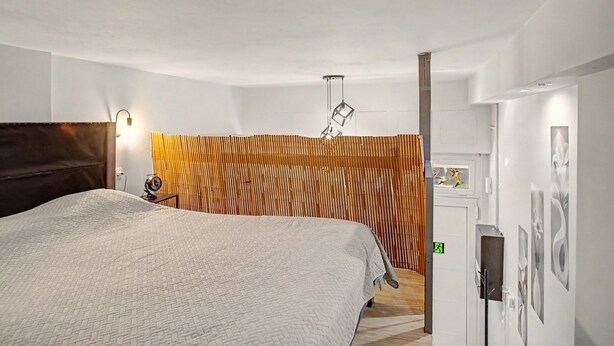 Une chambre d’hôtel comprenant un lit, un bureau, une lampe fixée au mur et un panneau décoratif mural.