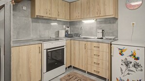 Une cuisine compacte avec des meubles en bois, un four encastré, un évier et un réfrigérateur orné de motifs floraux.