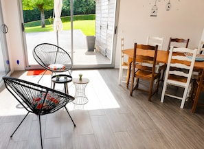 Ein modernes Zimmer mit einer Schiebeglastür, die auf eine Terrasse führt, einem Esstisch mit Stühlen und einem schwarzen Drahtgestellstuhl.