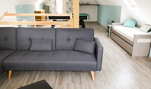 Una sala moderna con un sofá gris, una cama litera de madera, una mesita pequeña y un sofá cama.