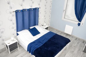 Ein Schlafzimmer mit Bett, Nachttischen, einem Fenster mit Vorhängen und einer Wand mit einem Rundmuster.