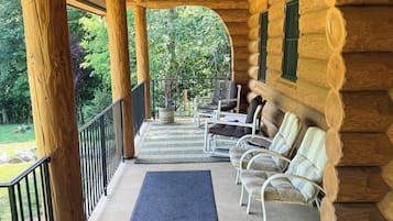 Une véranda couverte avec des poutres en bois, un paillasson noir et des chaises blanches.